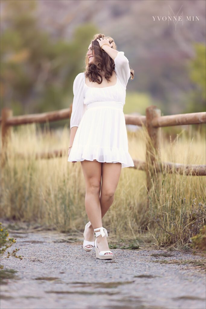 A senior girl from Legacy High School poses in a white dress at her senior photoshoot with Yvonne Min Photography at South Mesa Trailhead near Boulder, Colorado.